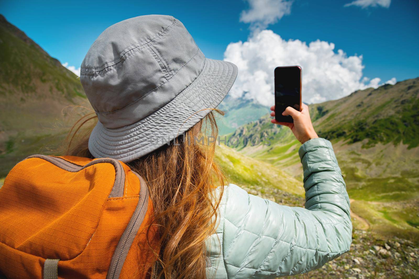 The girl is photographed on the phone picturesque views of mountains, forests and fluffy clouds, on a hike.