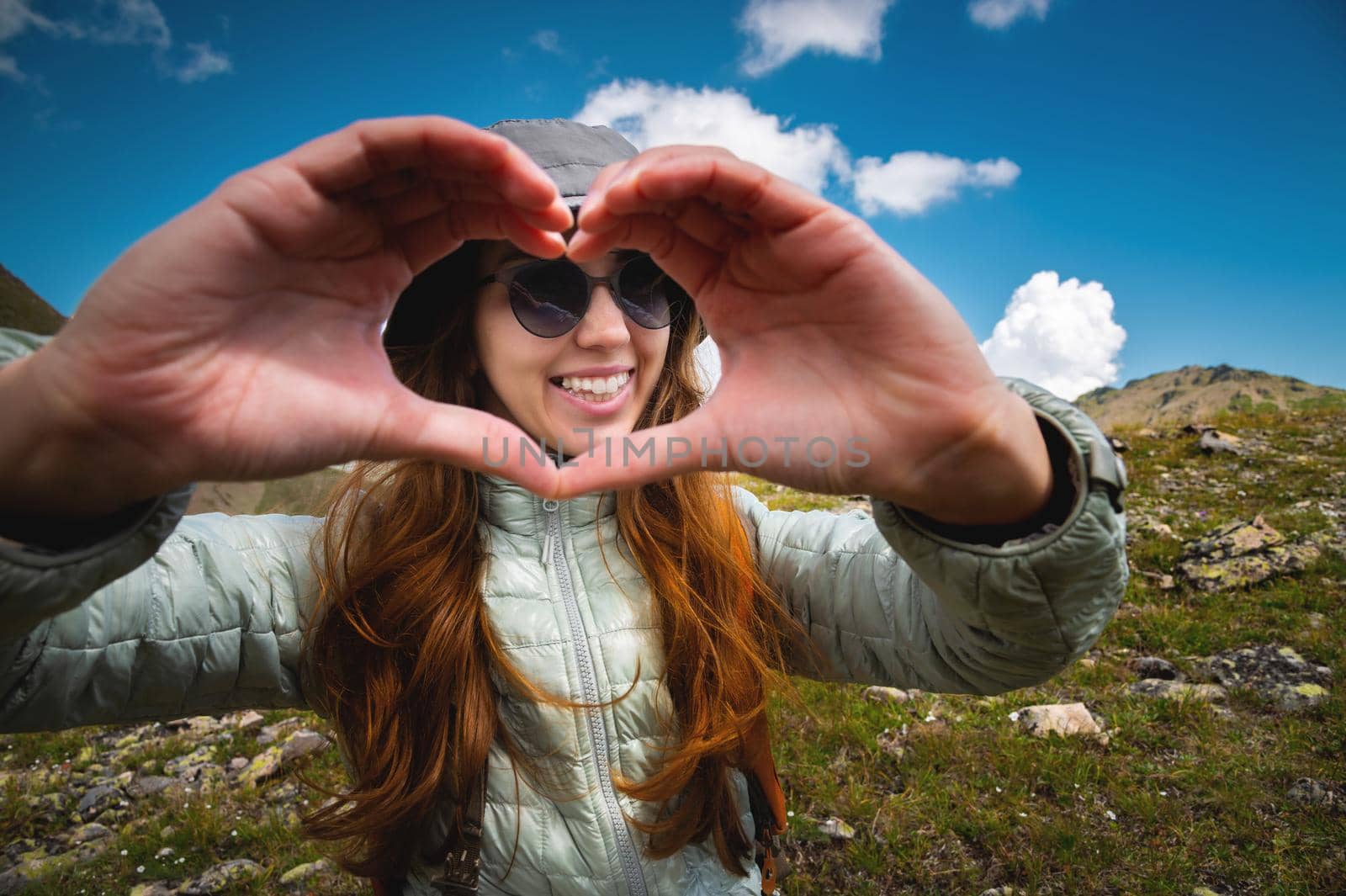 Hands in the shape of a love heart. A young woman makes a heart with her hands. Girl tourist on the top of the mountain with a backpack, the concept of love for nature.