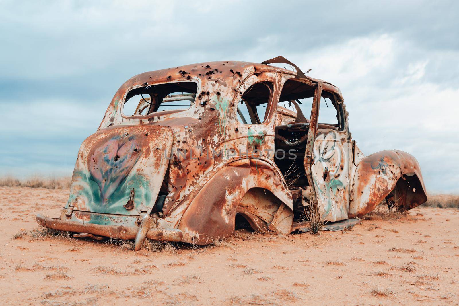 A vintage car sits abandoned and rusting in the harsh elements of Australian outback. Many rusted cars and other vehicles left behind can be found in journeys of the outback.