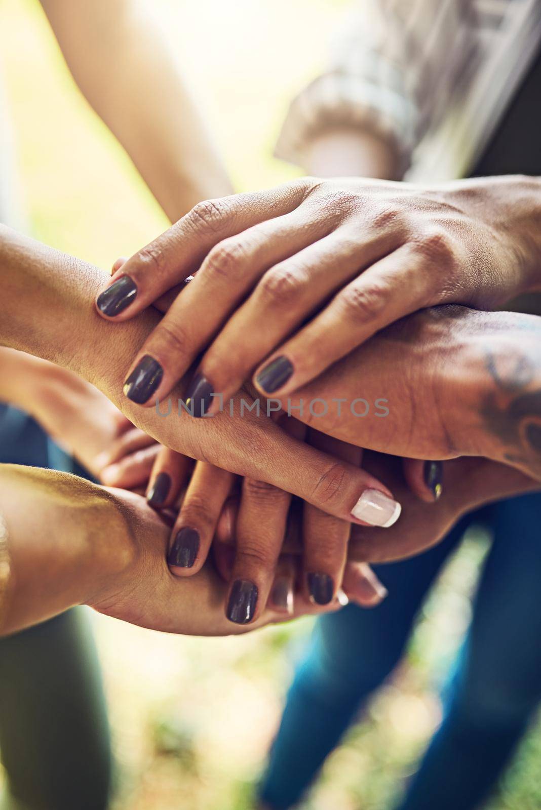 Together is better. Closeup shot of an unrecognizable group of people joining their hands in a huddle outdoors. by YuriArcurs