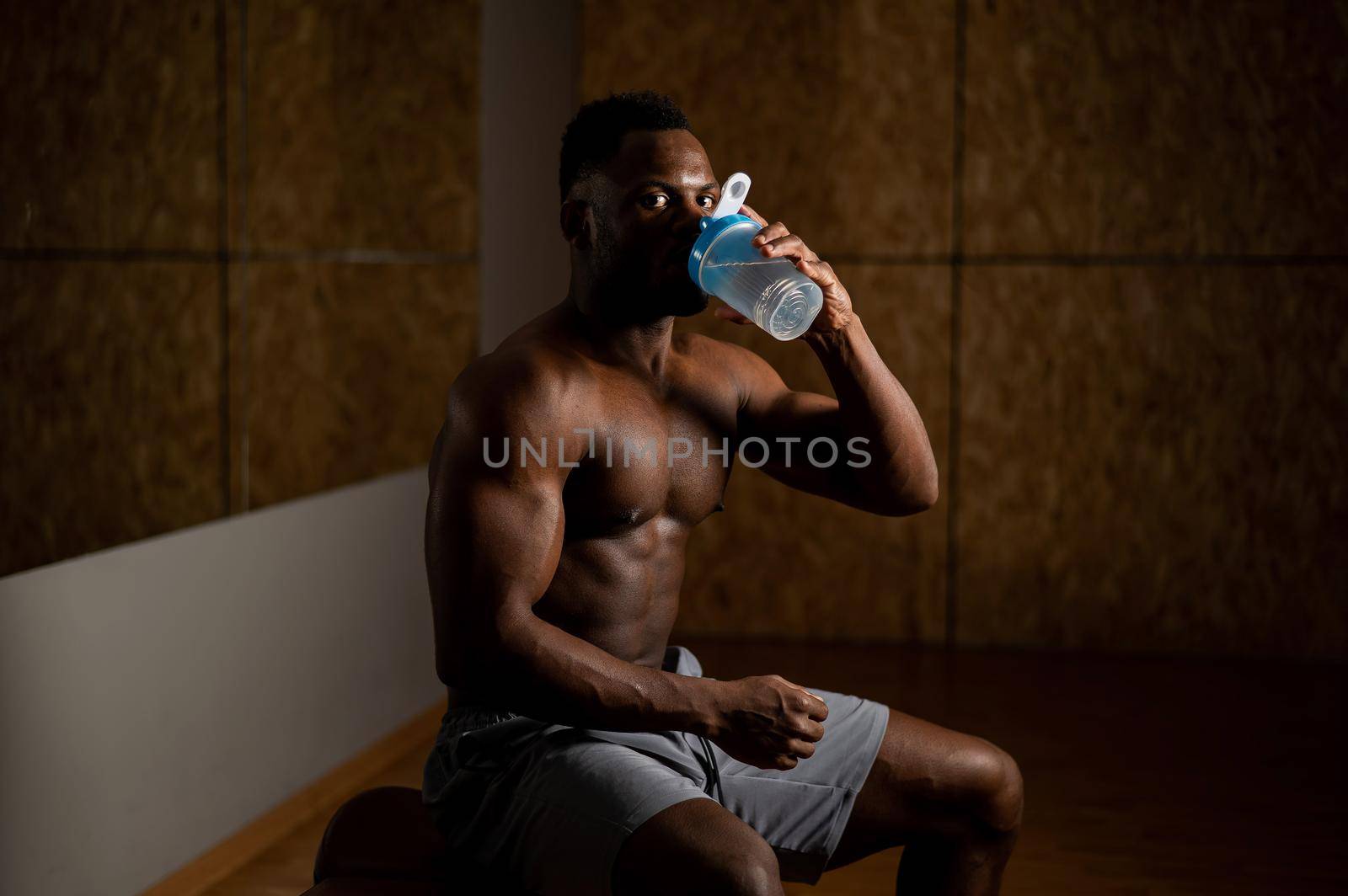 Shirtless african american man drinking from a shaker in the gym