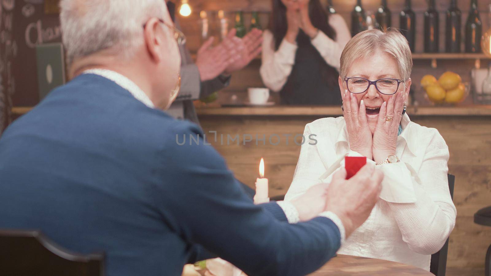 Senior man giving diamond engagement ring in little red box to his woman by DCStudio