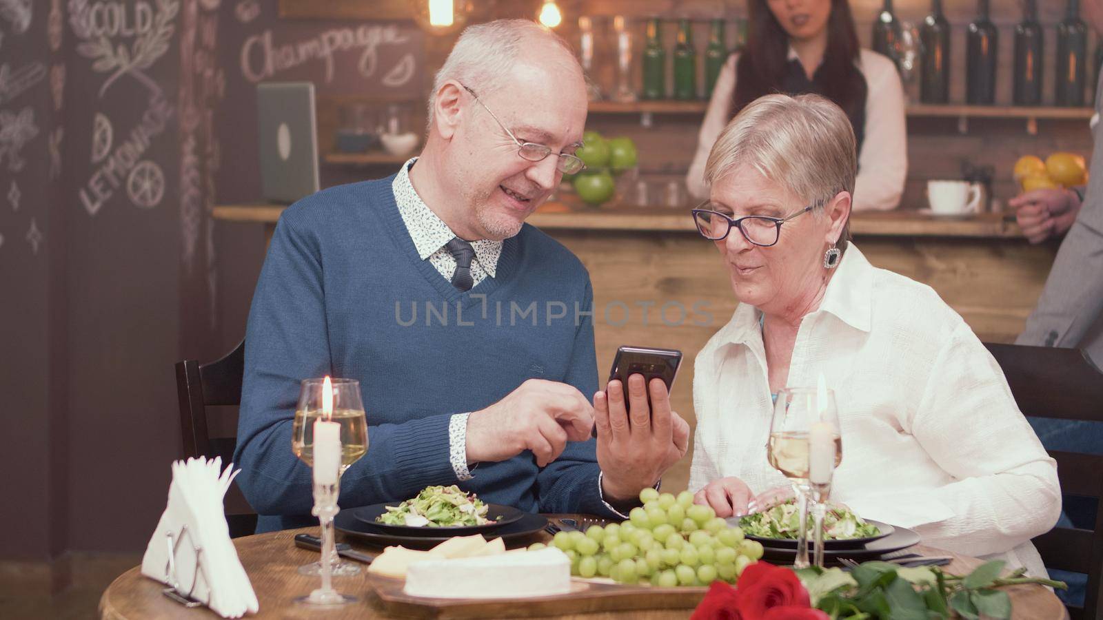 Senior man showing something on his phone to his wife in a restaurant. Cheerful senior couple. Romantic couple.