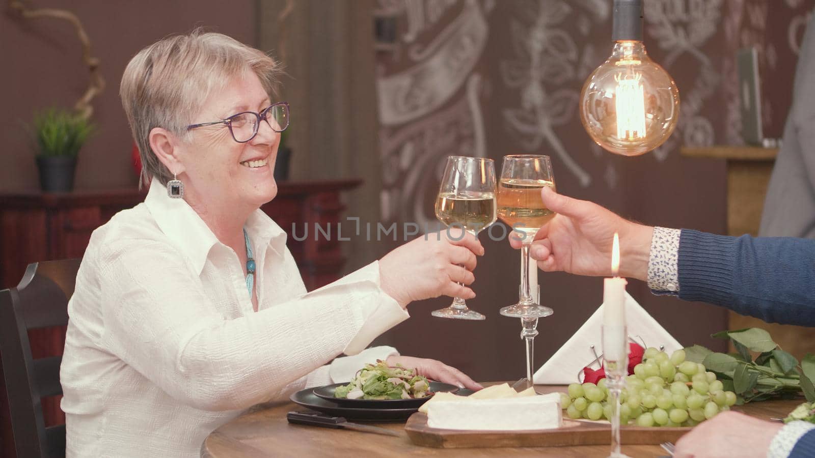 Senior woman clinking glasses with his husband durring thier date. Romantic couple. Cheerful couple. Mand and woman in their sixties.