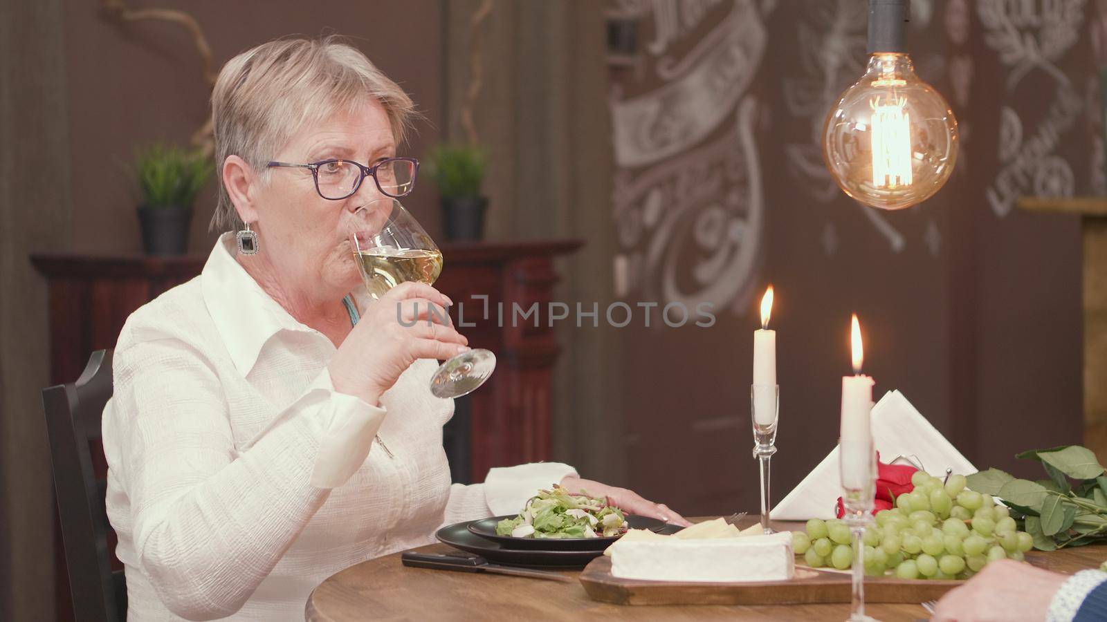 Lovely old lady drinking wine during a romantic date. Romantic old woman. Woman in her sixties.