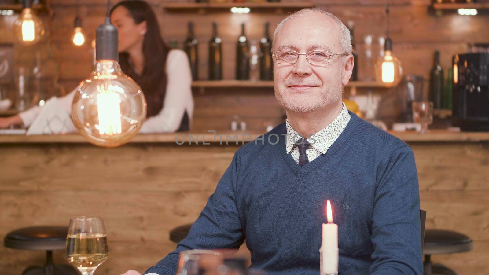Senior man at restaurant table smiling to the camera by DCStudio