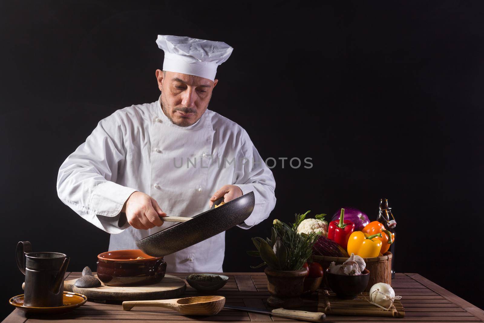 Male chef in white uniform preparing food plate with vegetables before serving while working in a restaurant kitchen