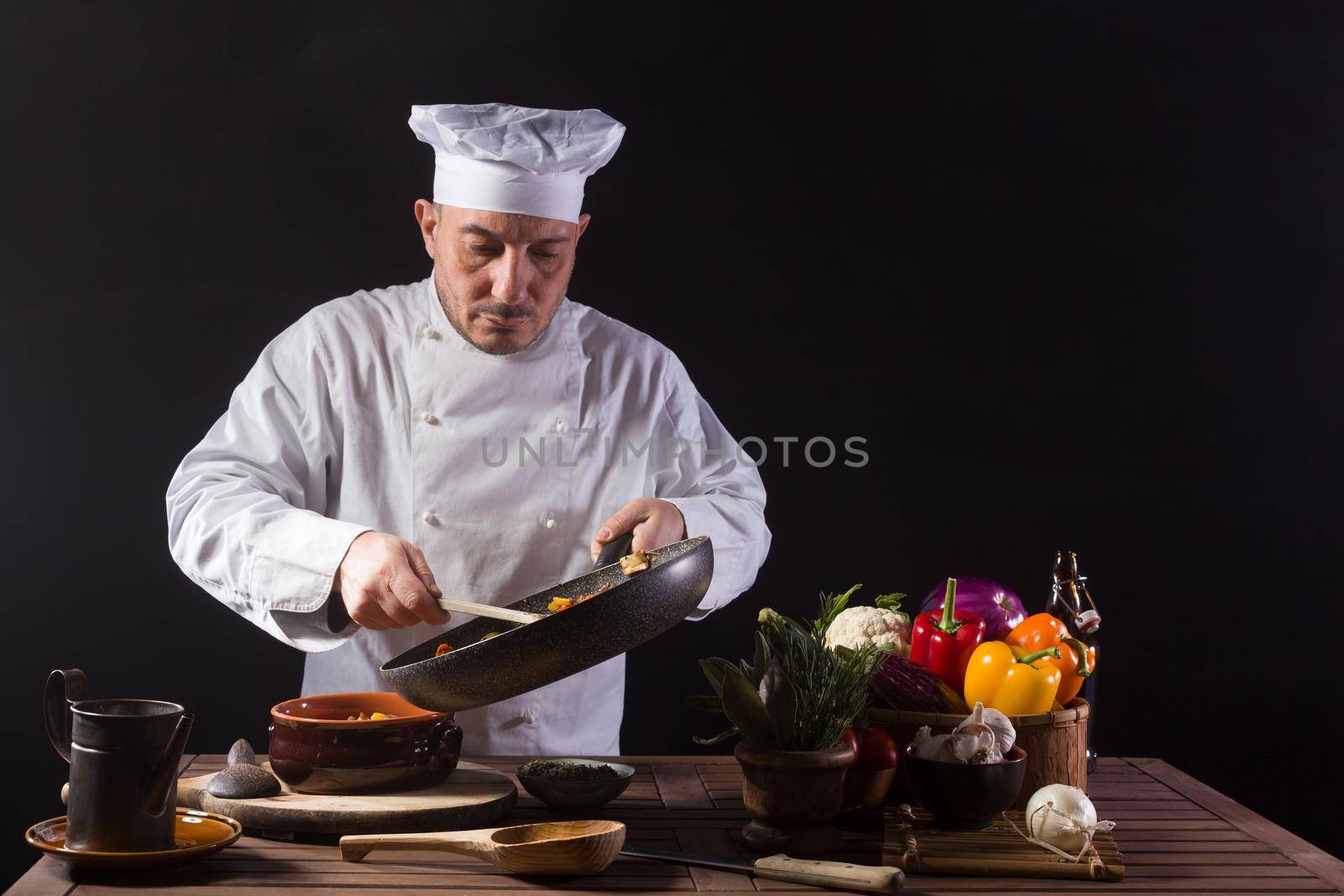 Male chef in white uniform preparing food plate with vegetables before serving while working in a restaurant kitchen