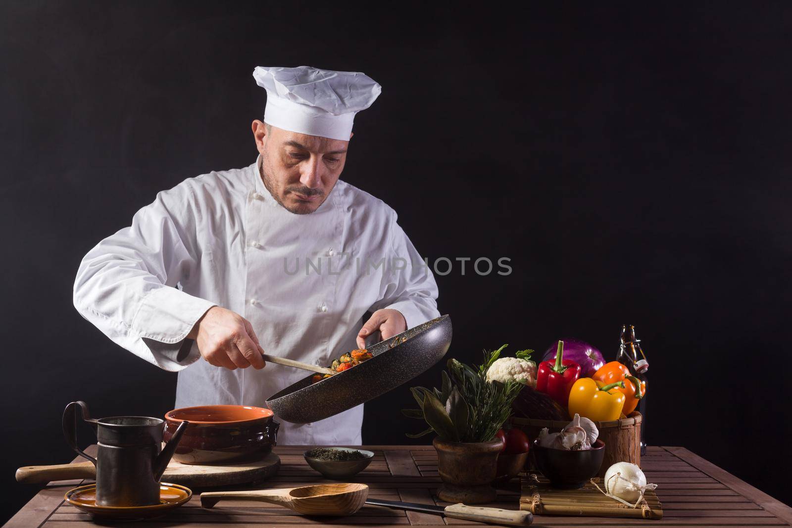 Male chef in white uniform preparing food plate with vegetables before serving while working in a restaurant kitchen