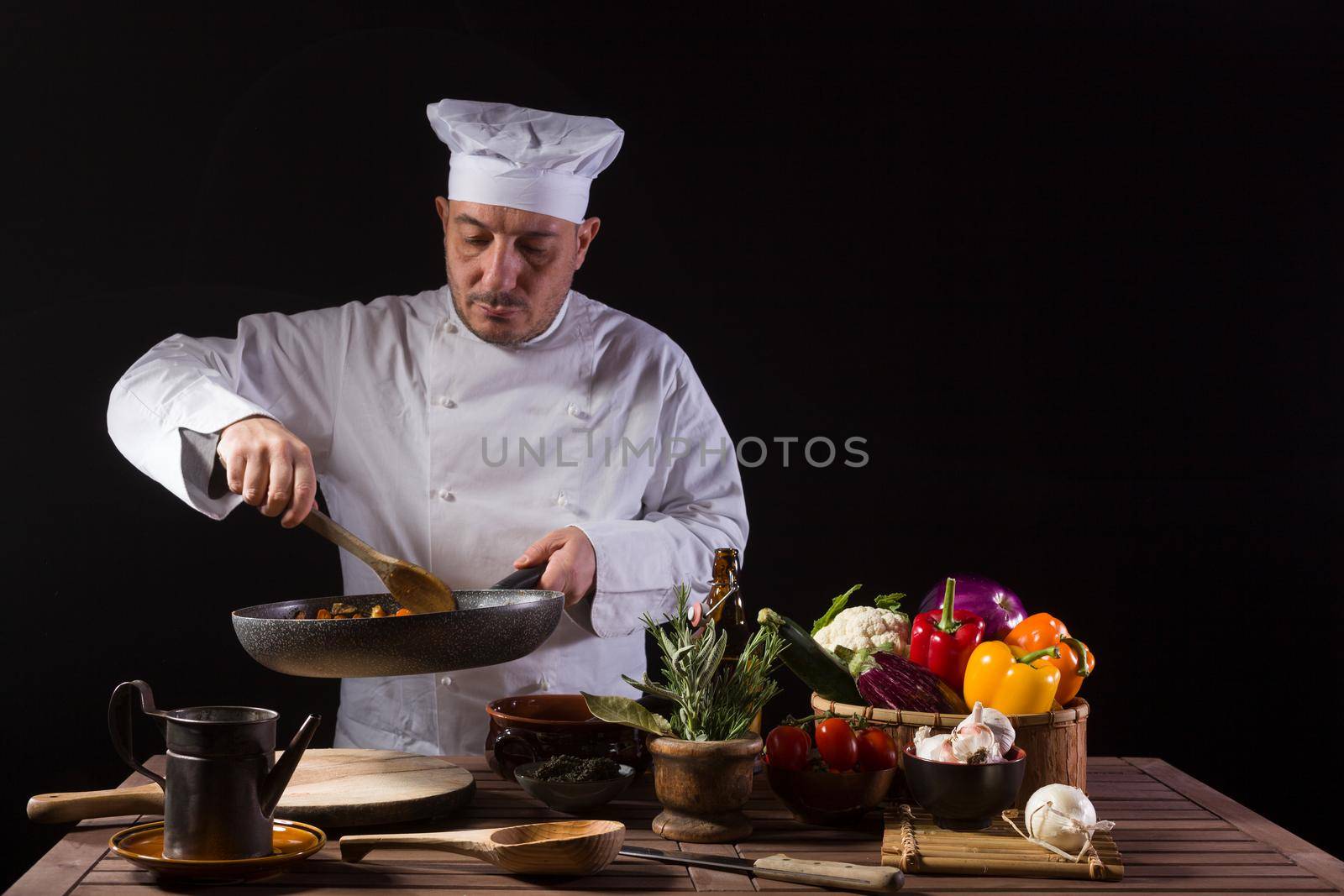 Chef in white uniform and hat with ladle mixes the ingredients onto the cooking pan by bepsimage