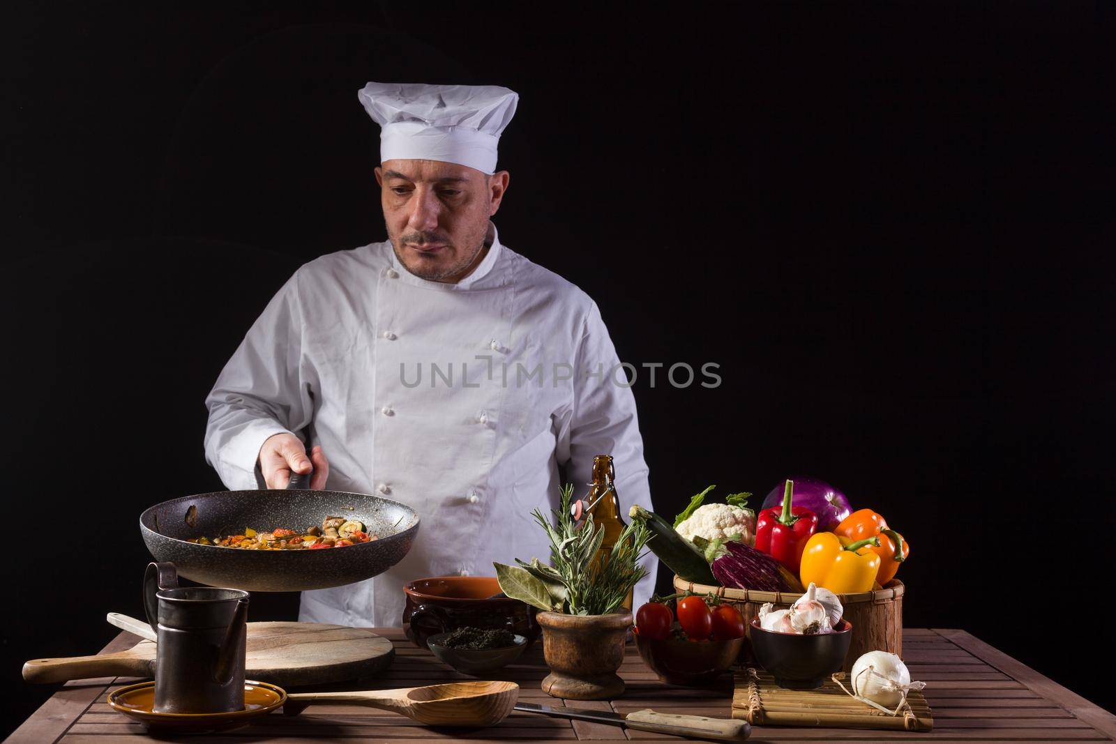 Chef in white uniform and hat with looking the cooking pan before serving while working in a restaurant kitchen