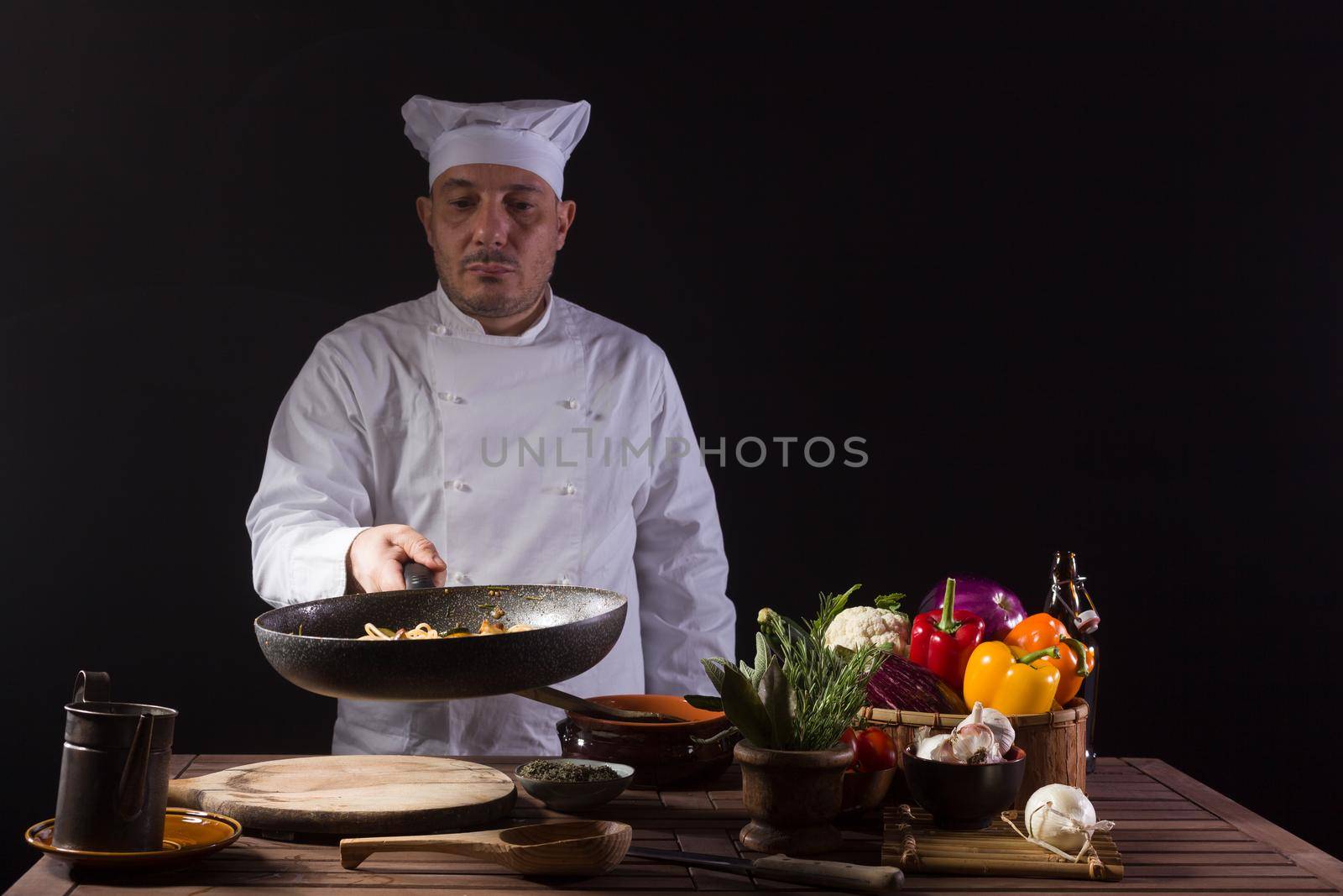 Chef in white uniform and hat with looking the cooking pan before serving while working in a restaurant kitchen