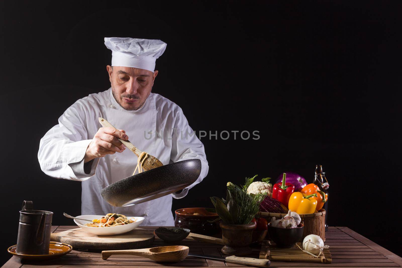 Male chef in white uniform prepares spaghetti with vegetables on the dish before serving while working in a restaurant kitchen