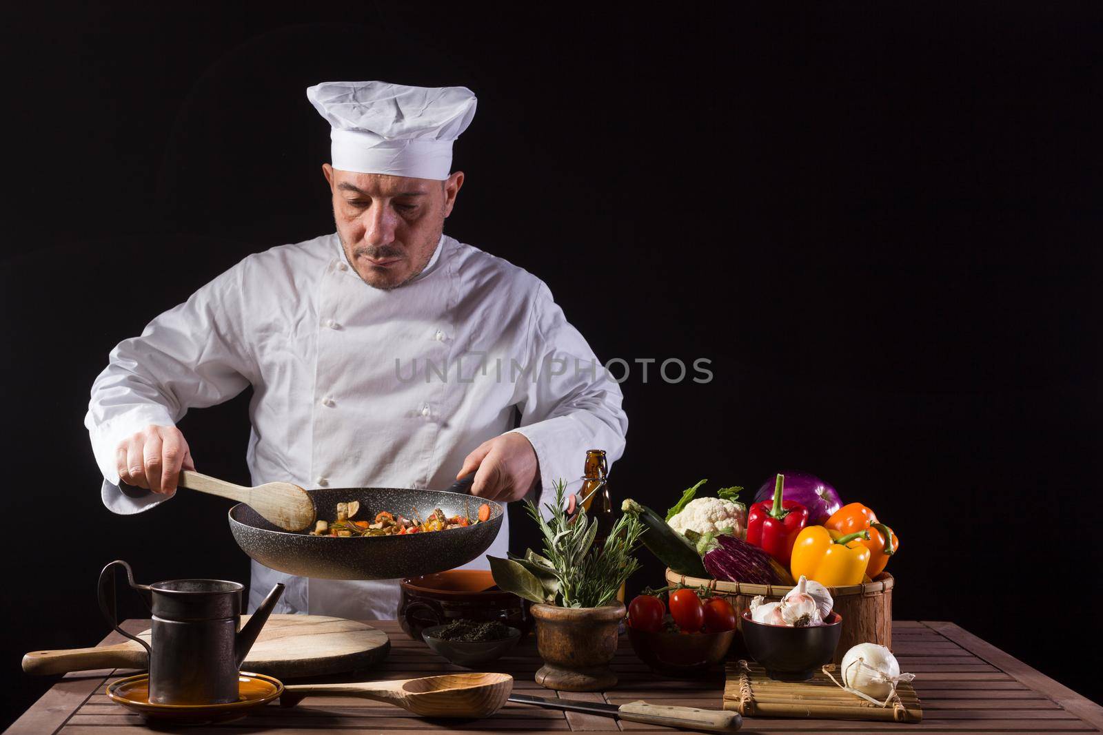 Chef in white uniform and hat with ladle mixes the ingredients onto the cooking pan by bepsimage