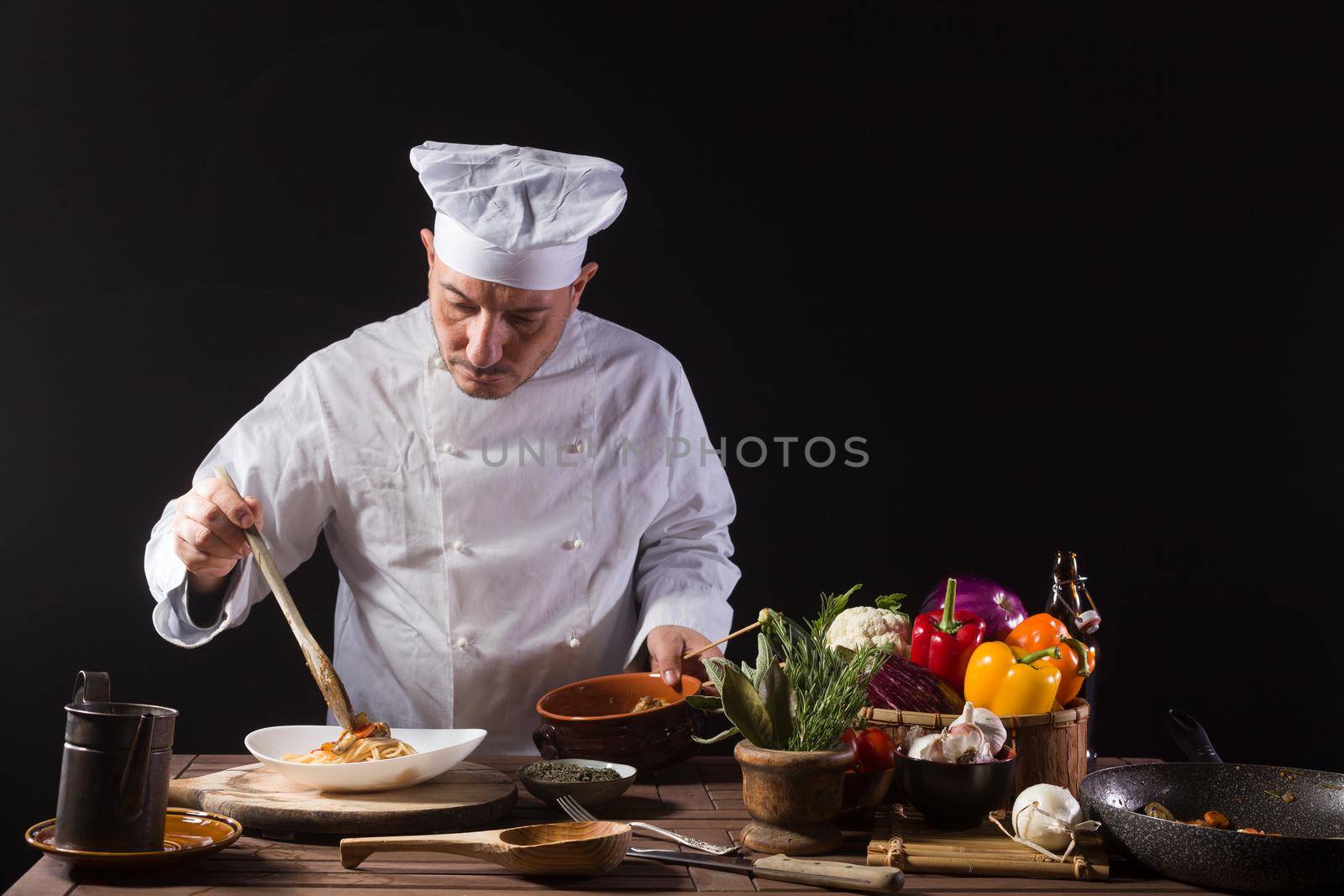 Male chef in white uniform prepares spaghetti with vegetables on the dish before serving while working in a restaurant kitchen