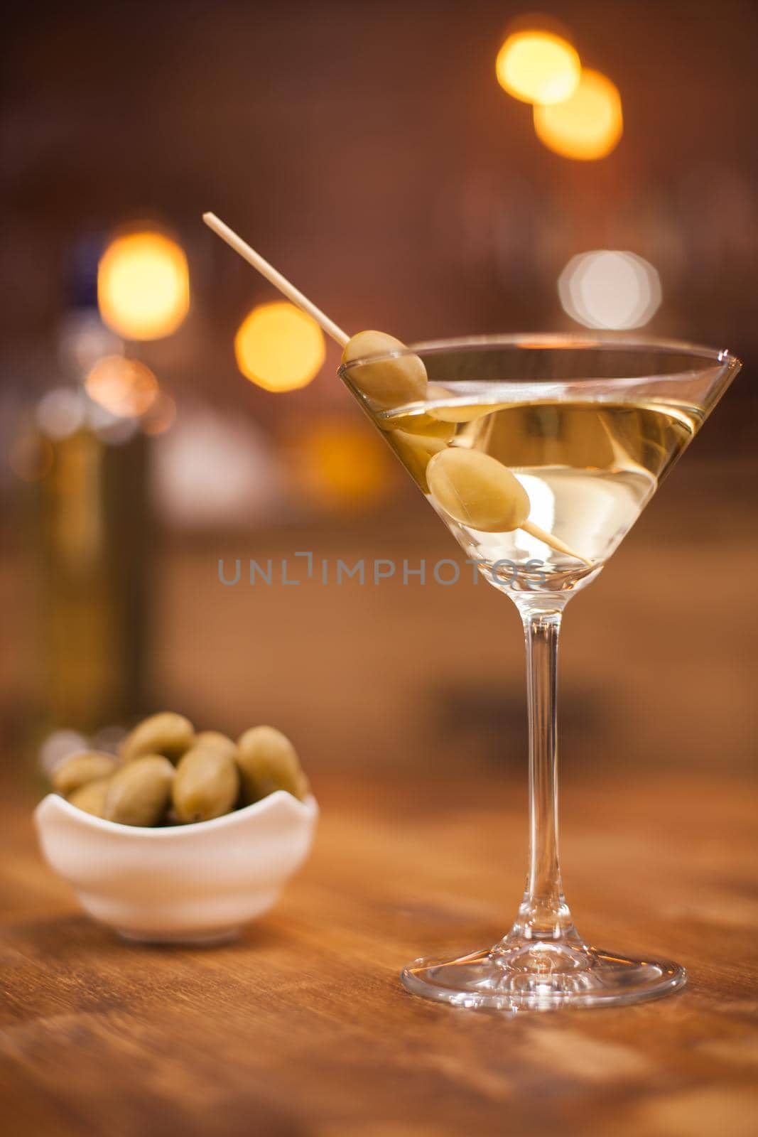 Tasty glass of dry martini with olives on a stick and a bowl of olives next to it. Relaxing with a glass of martini.