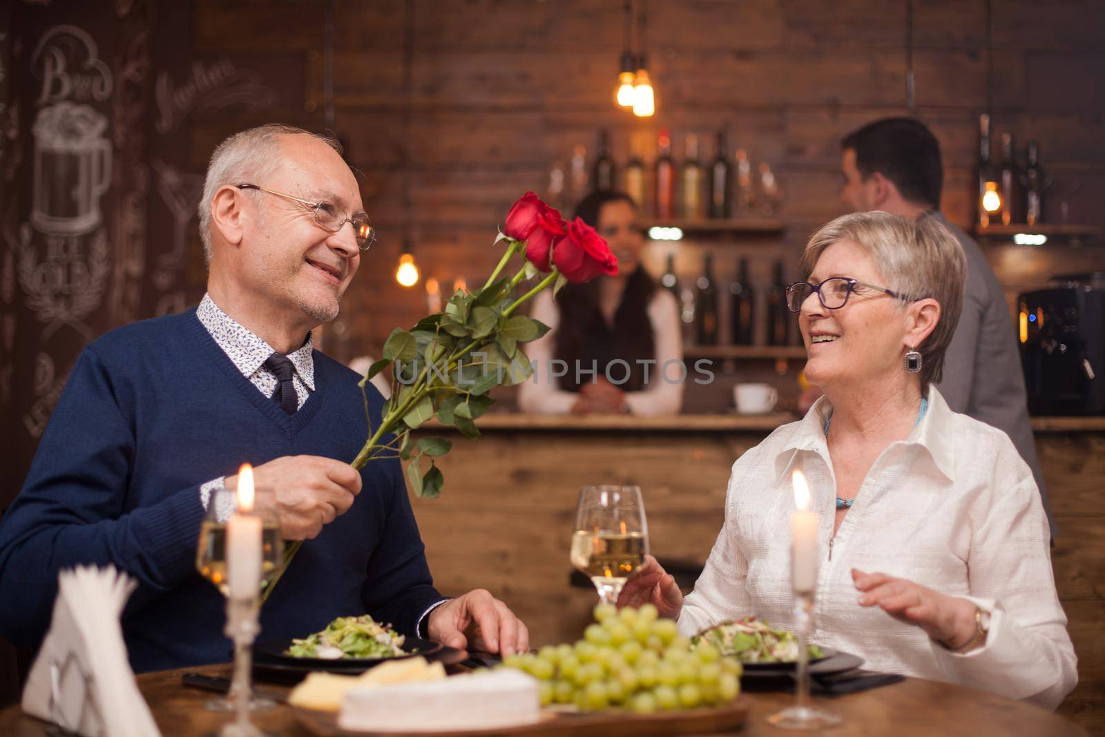 Husband in his sixties giving roses to his wife in a restaurant. Happy wife. Old people smiling. Mature man and woman.