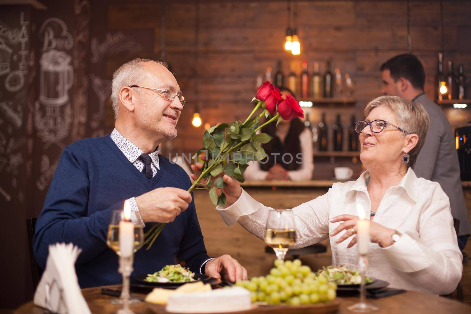 Woman in her sixties happy to recieve roses from her husband during dinner by DCStudio
