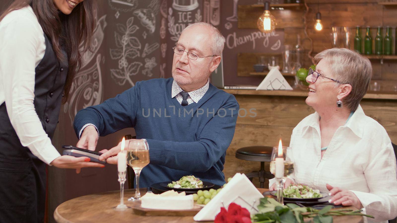 Senior man paying the bill with his credit card in a restaurant. Senior couple at the restaurant. Romantic old couple.