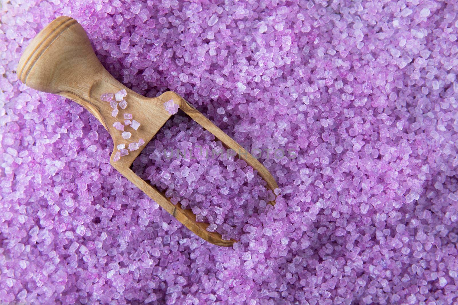 Purple bath salts with wooden scoop filling frame and viewed from above
