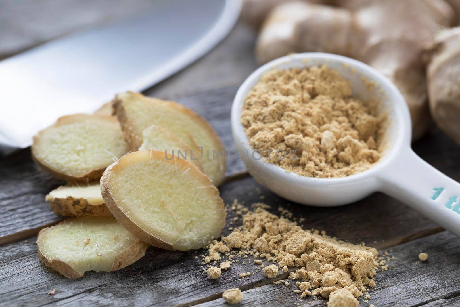 Ginger root, slices, and powder with knife in background.