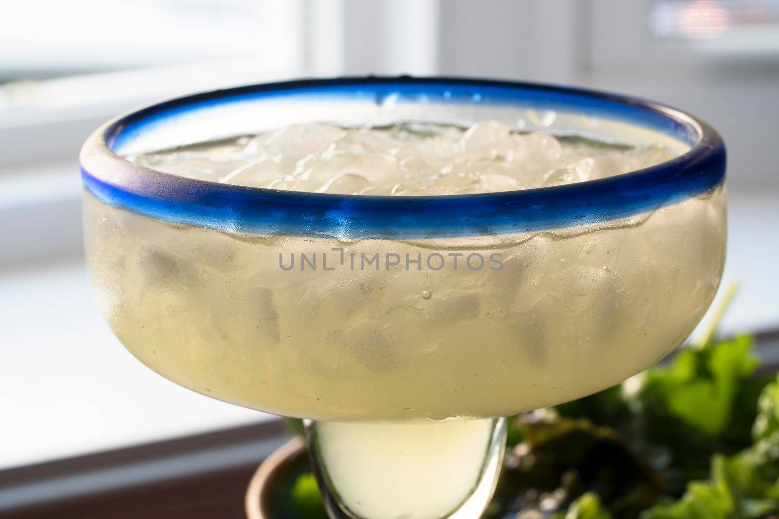 Close up of margarita on ice in glass with blue rim.