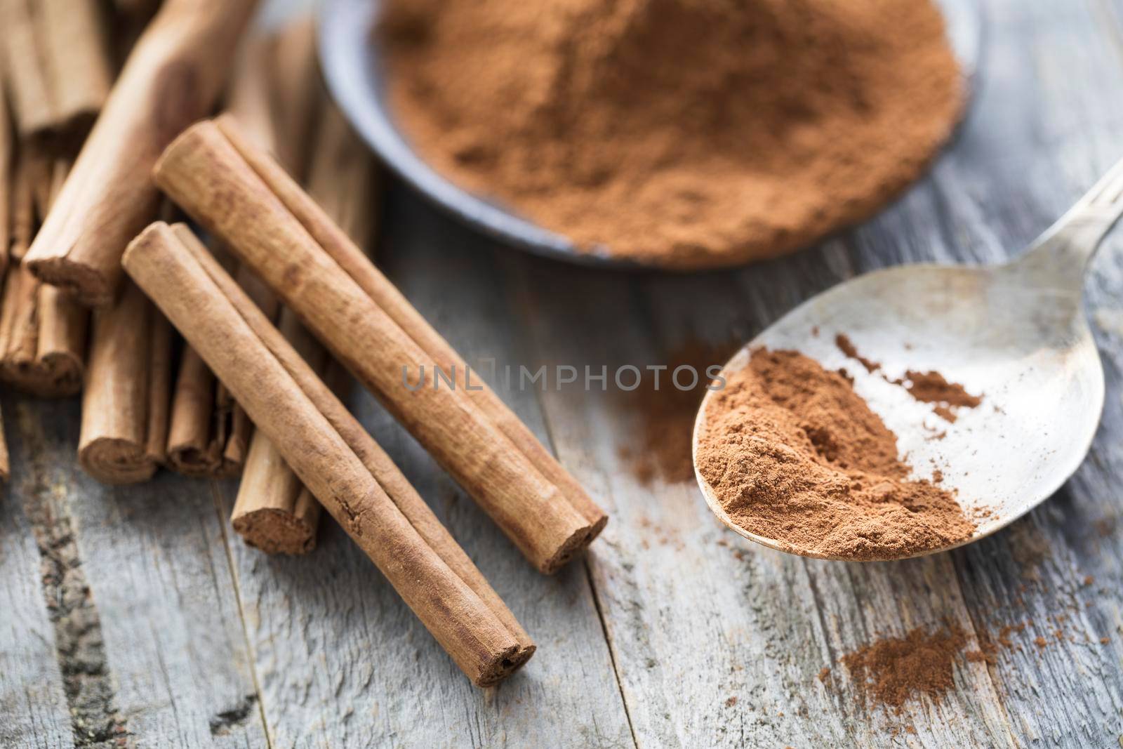 Close up of ground cinnamon on spoon with whole cinnamon sticks.