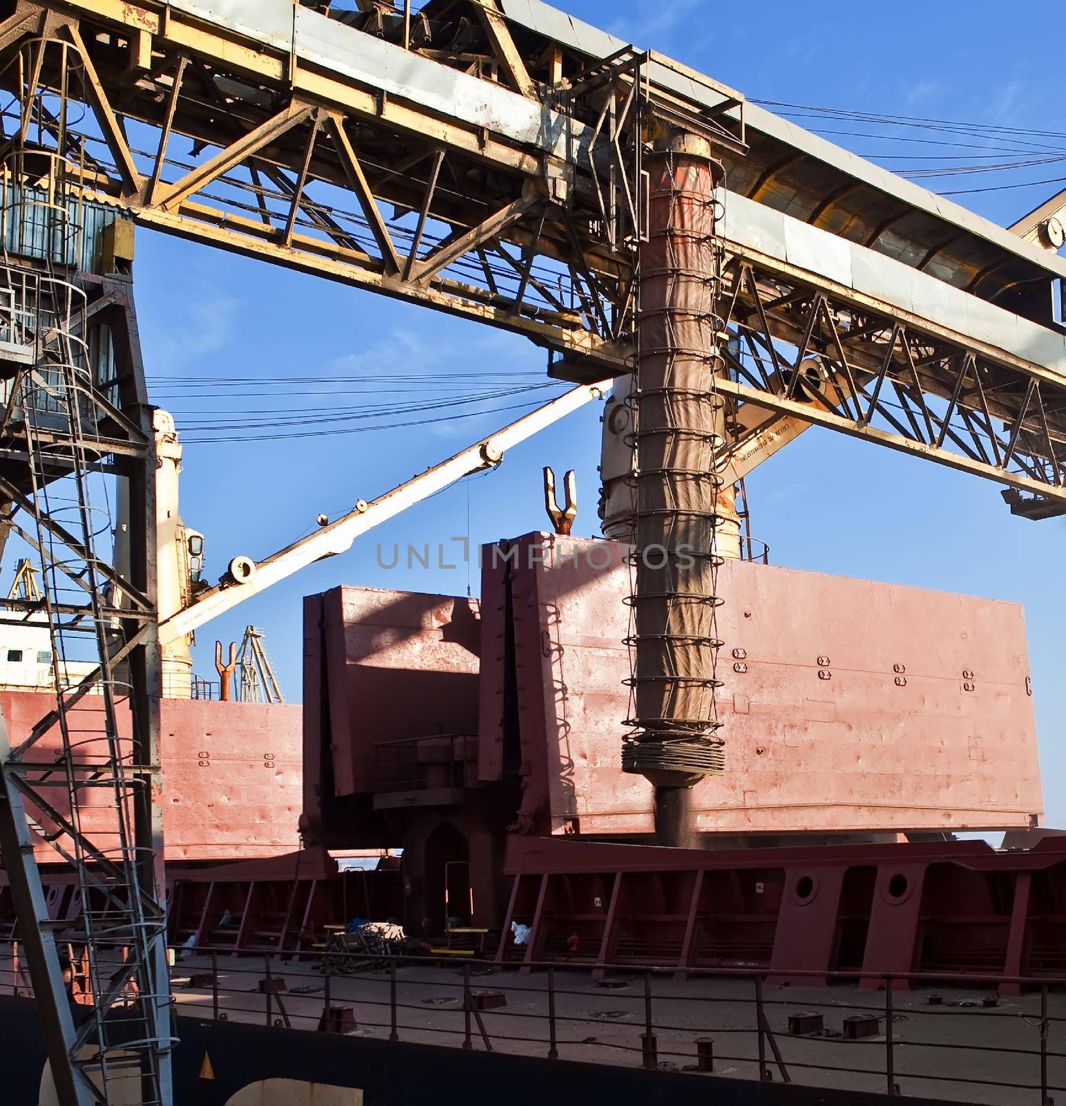 Loading grain into holds of sea cargo vessel in seaport from grain storage. by sarymsakov