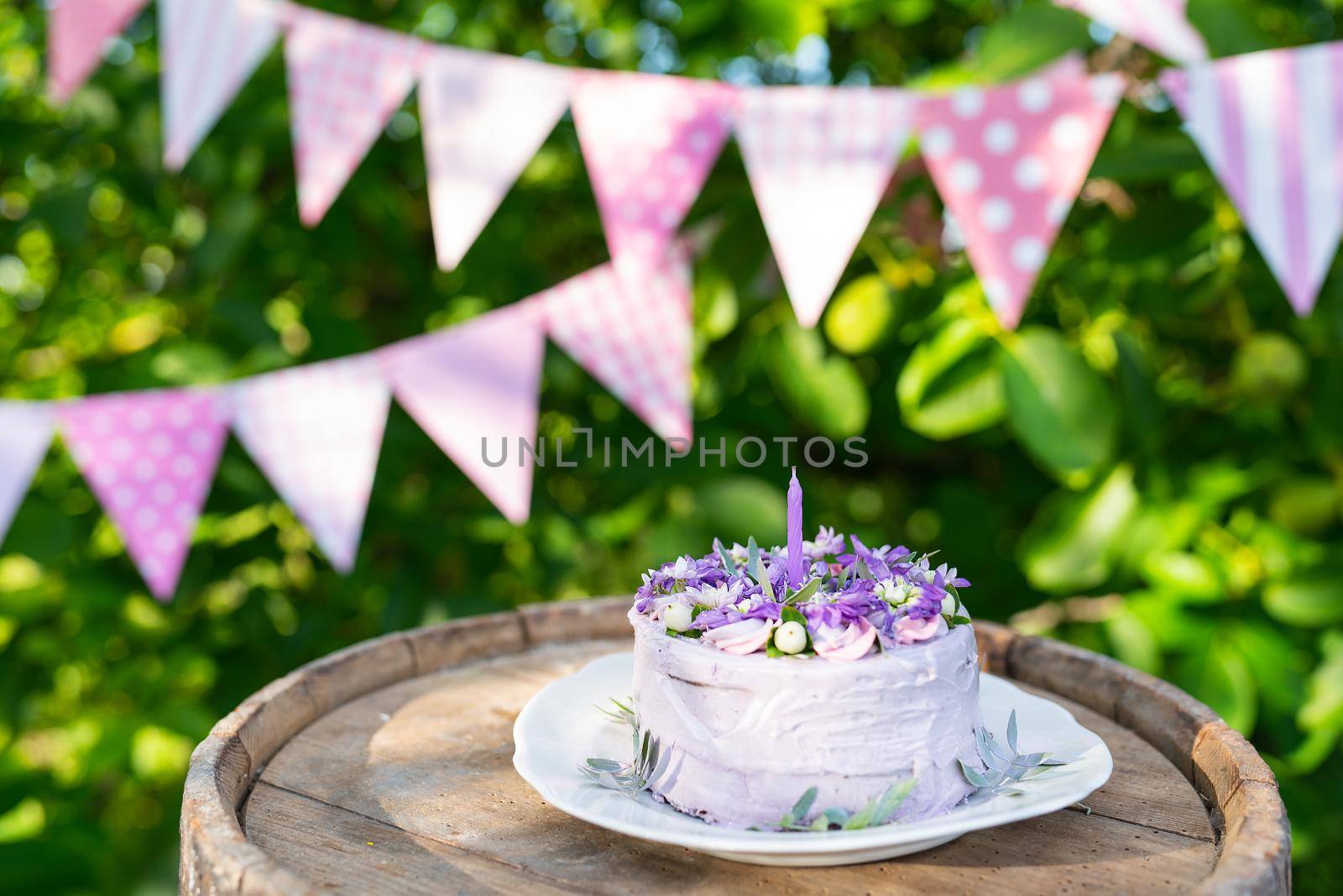 Very beautiful bento cake with purple, veri peri, matthiola flowers with green leaves, candles in the cake on the background of pink flags. Birthday. Horizontal photo. by sfinks