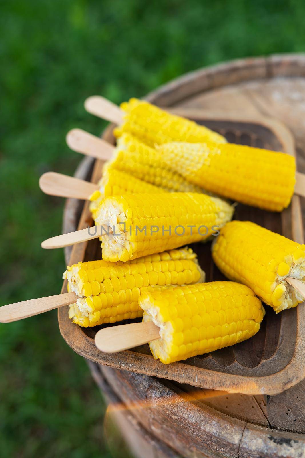 Boiled sweet corn with salt and butter on a stick on a wooden plate. Summer vegan dinner or snack, preparing for the grill. Vertical photo