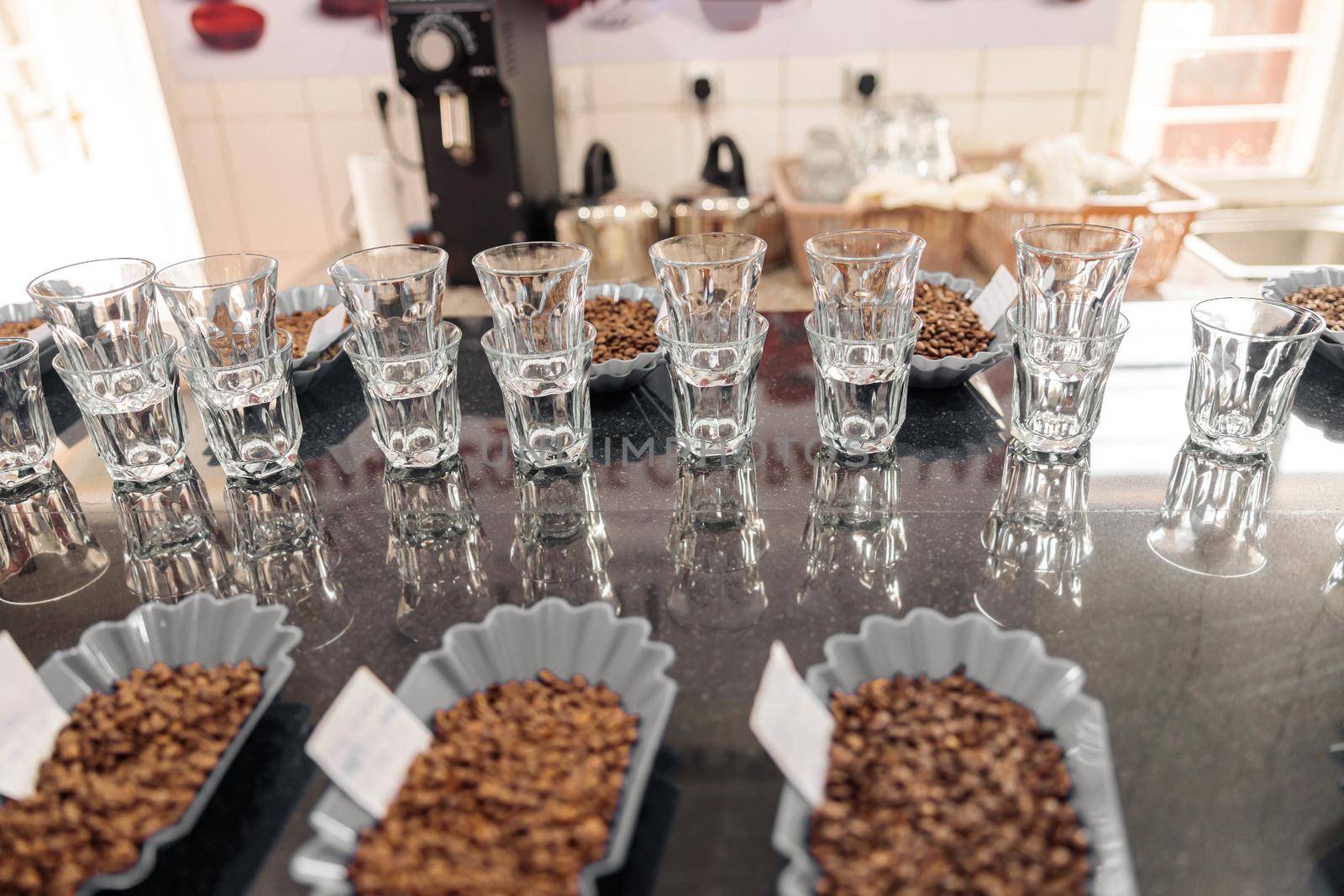 Empty water glasses and bowls with different types of coffee beans in a row on a tasting table