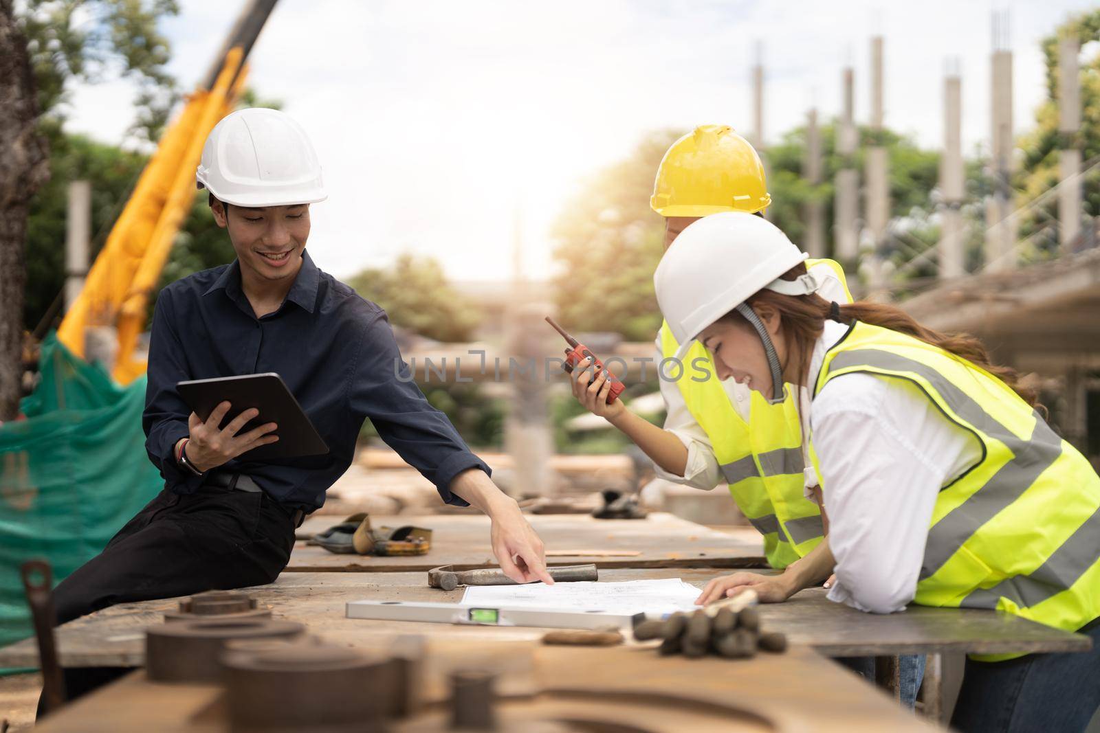 Young asian architects and engineer discussing blueprints at construction site.