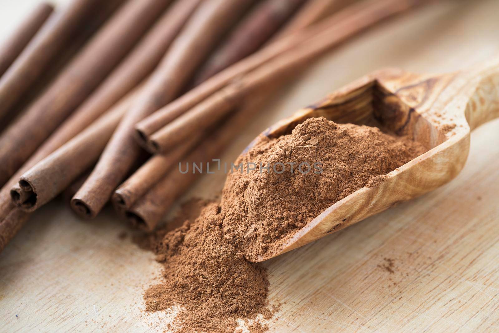 Close up of wooden scoop full of cinnamon powder next to cinnamon sticks.