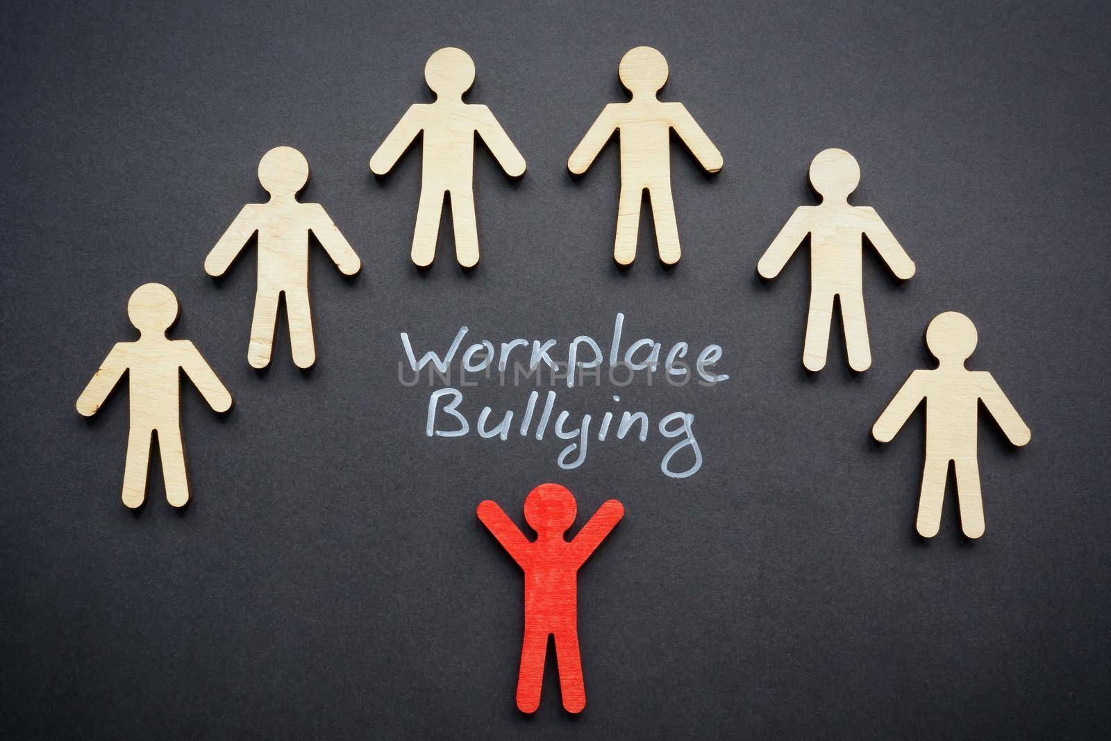 Workplace bullying and wooden figurines on the dark surface. by designer491