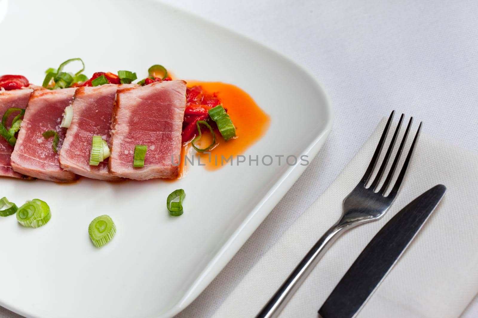 Slices of Tuna on a plate, onions and pepper sauce