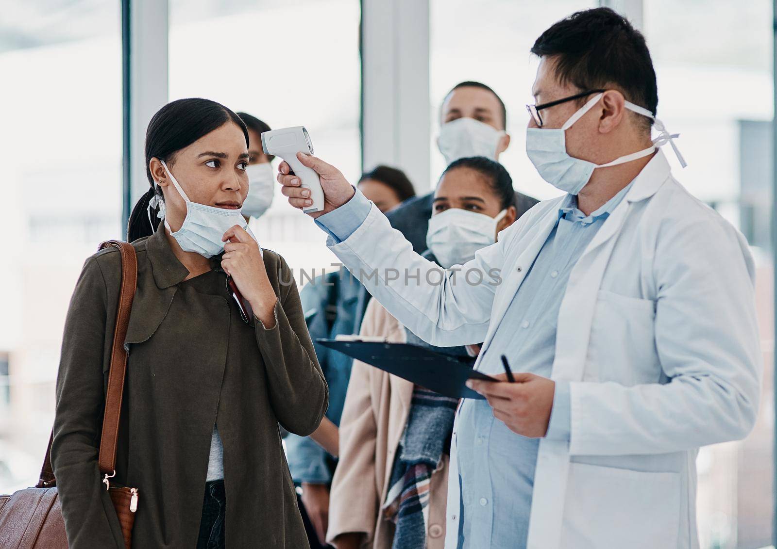 Travel medical healthcare worker testing covid temperature at airport using infrared thermometer. Professional doctor doing a coronavirus check up on a woman at an office entrance by YuriArcurs