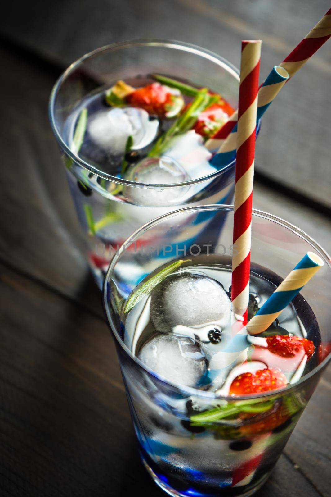 Detox summer drink with rosemary, strawberry, and bilberry with bright color straws on dark wooden table