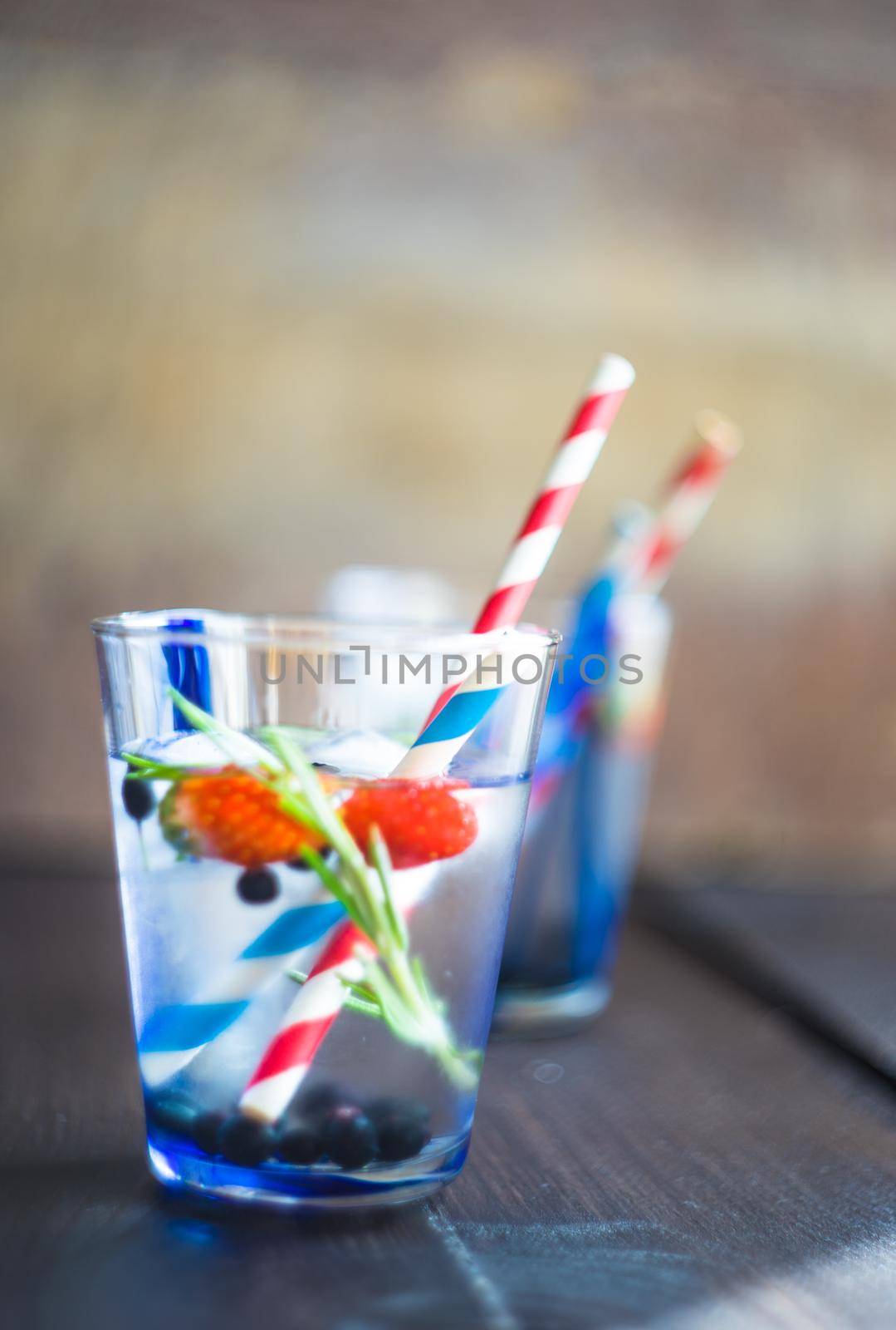 Detox summer drink with rosemary, strawberry, and bilberry with bright color straws on dark wooden table