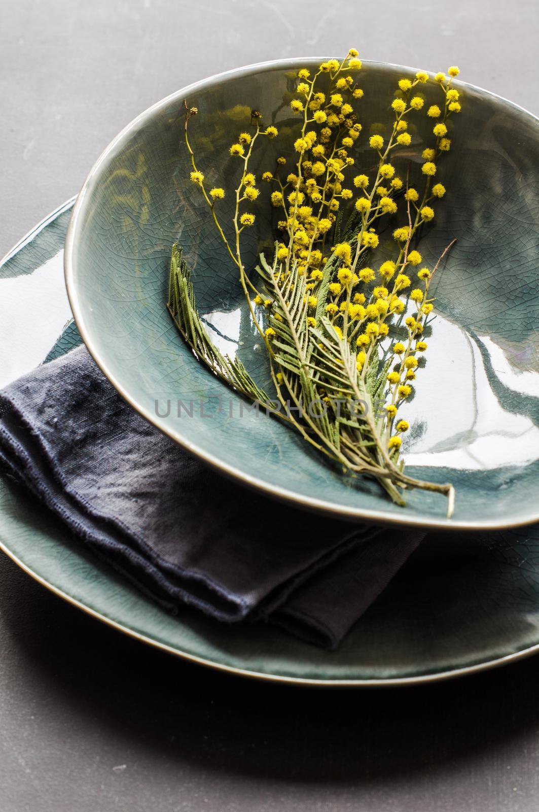Festive table setting for Easter dinner with bright easter eggs and mimosa flowers on rustic plate