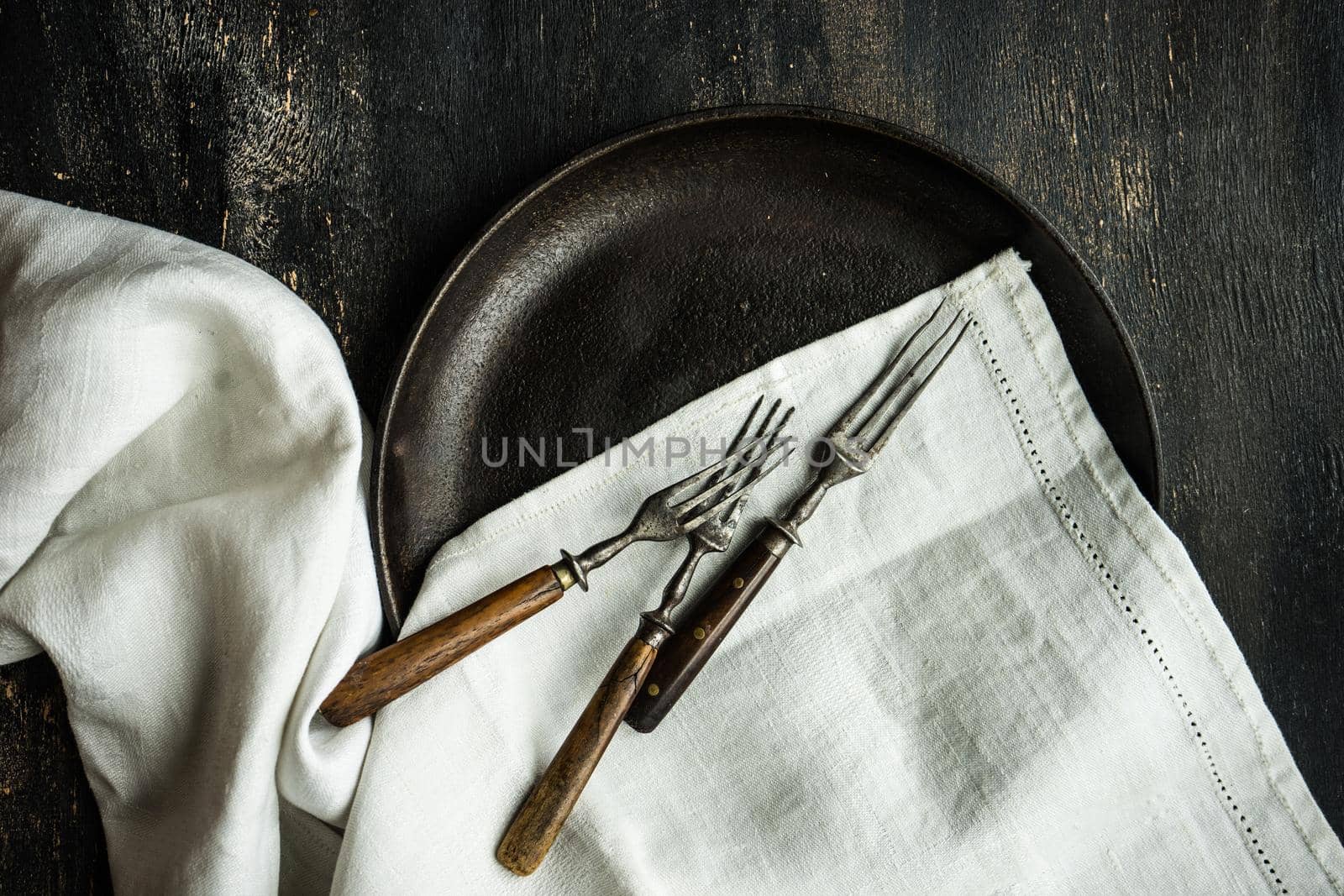 Rustic table setting ith vintage metal plate and cutlery on dark wooden table