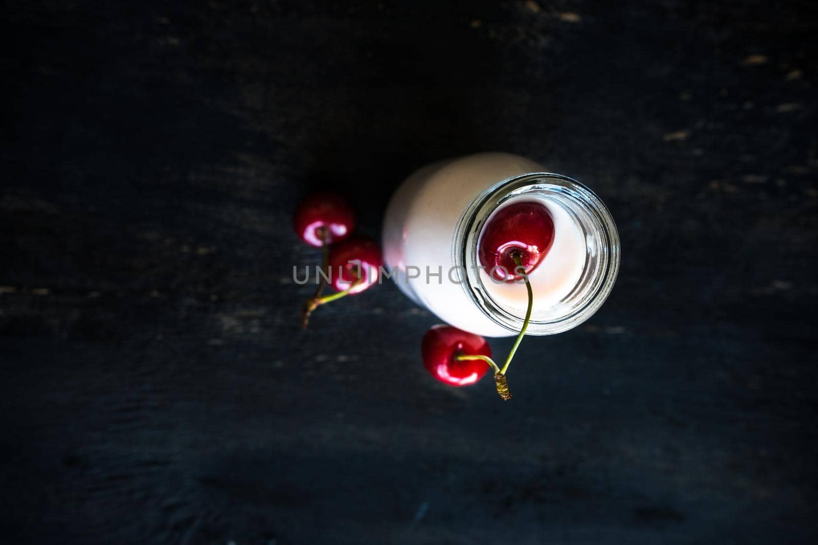 Bottle with yogurt and cherries on dark wooden table with copyspace