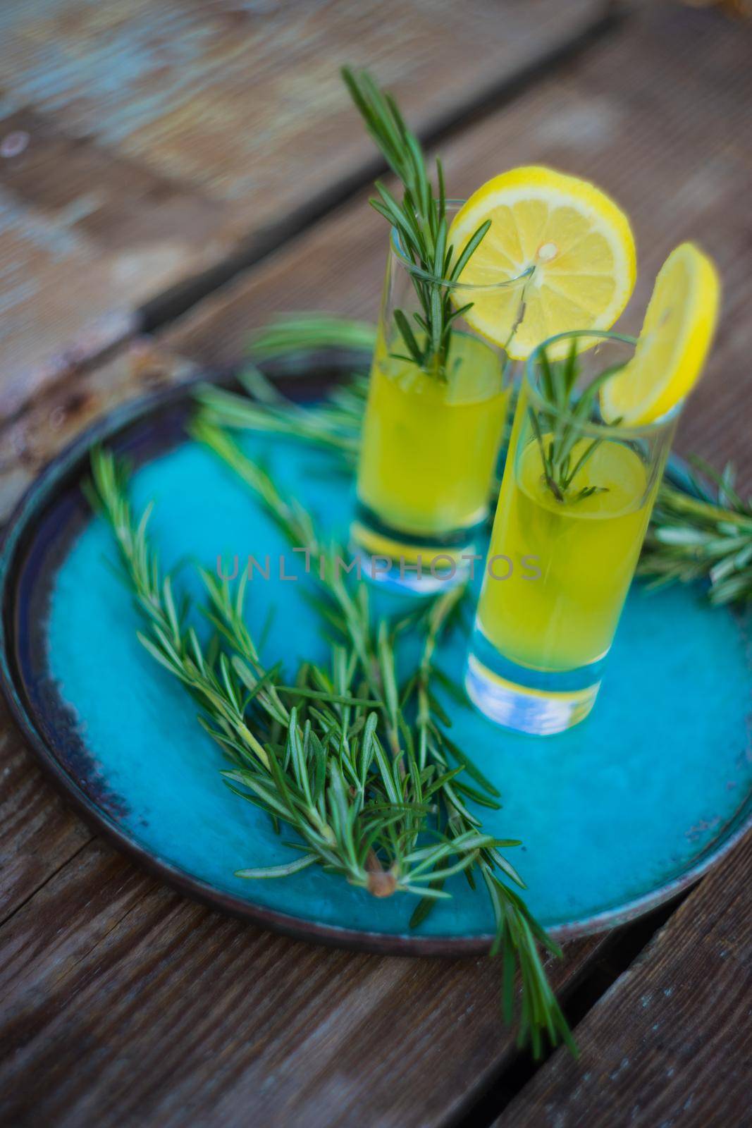 Traditional italian lemon alcohol drink limoncello with pieces of lemon and rosemary herb on dark wooden table