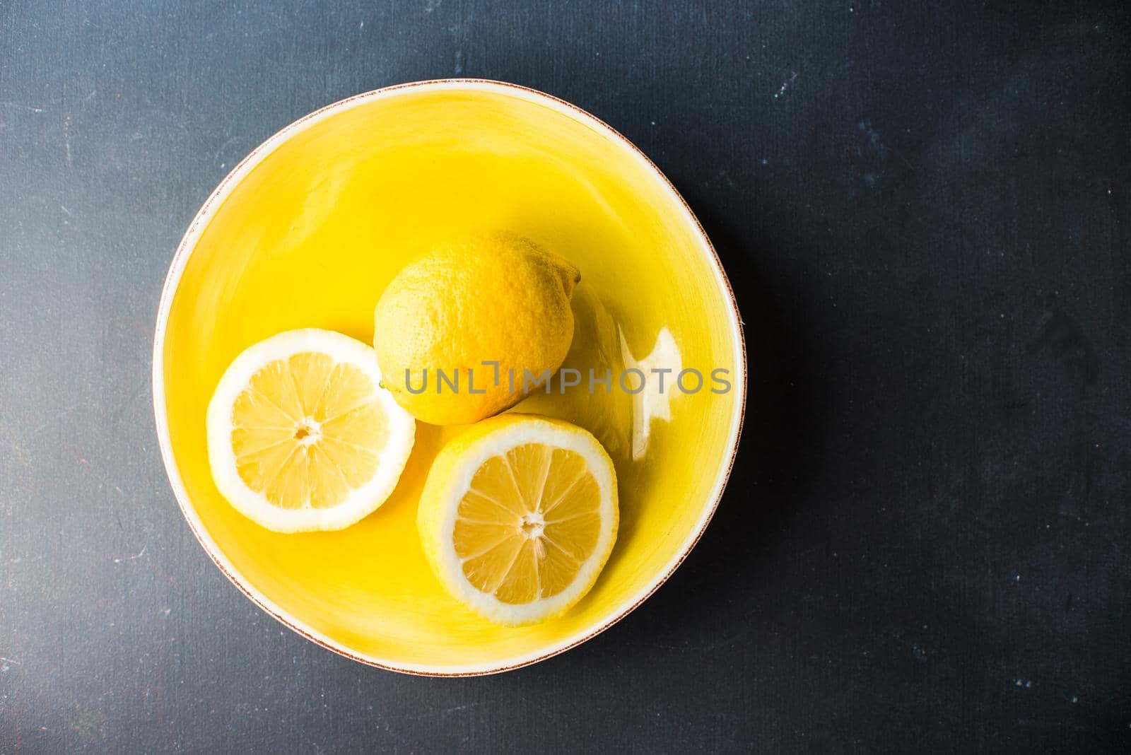 Fresh organic lemons in a bright yellow ceramic bowl on dark background