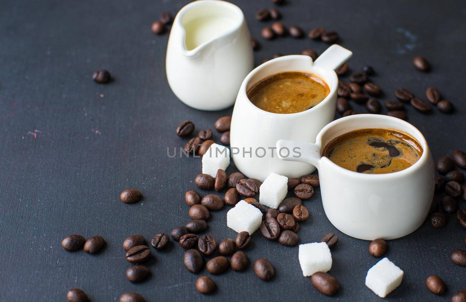 Mug with black coffee, coffee beans, milk and sugar on dark wooden table