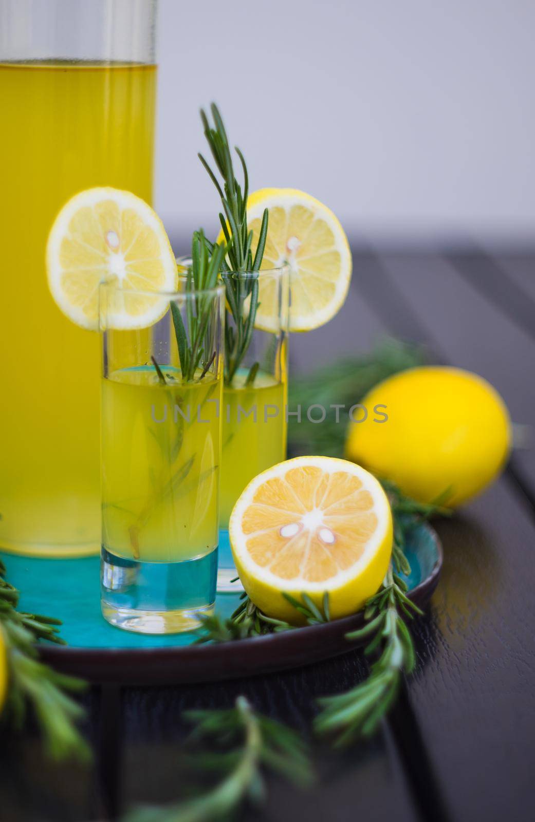 Traditional italian lemon alcohol drink limoncello with pieces of lemon and rosemary herb on dark wooden table
