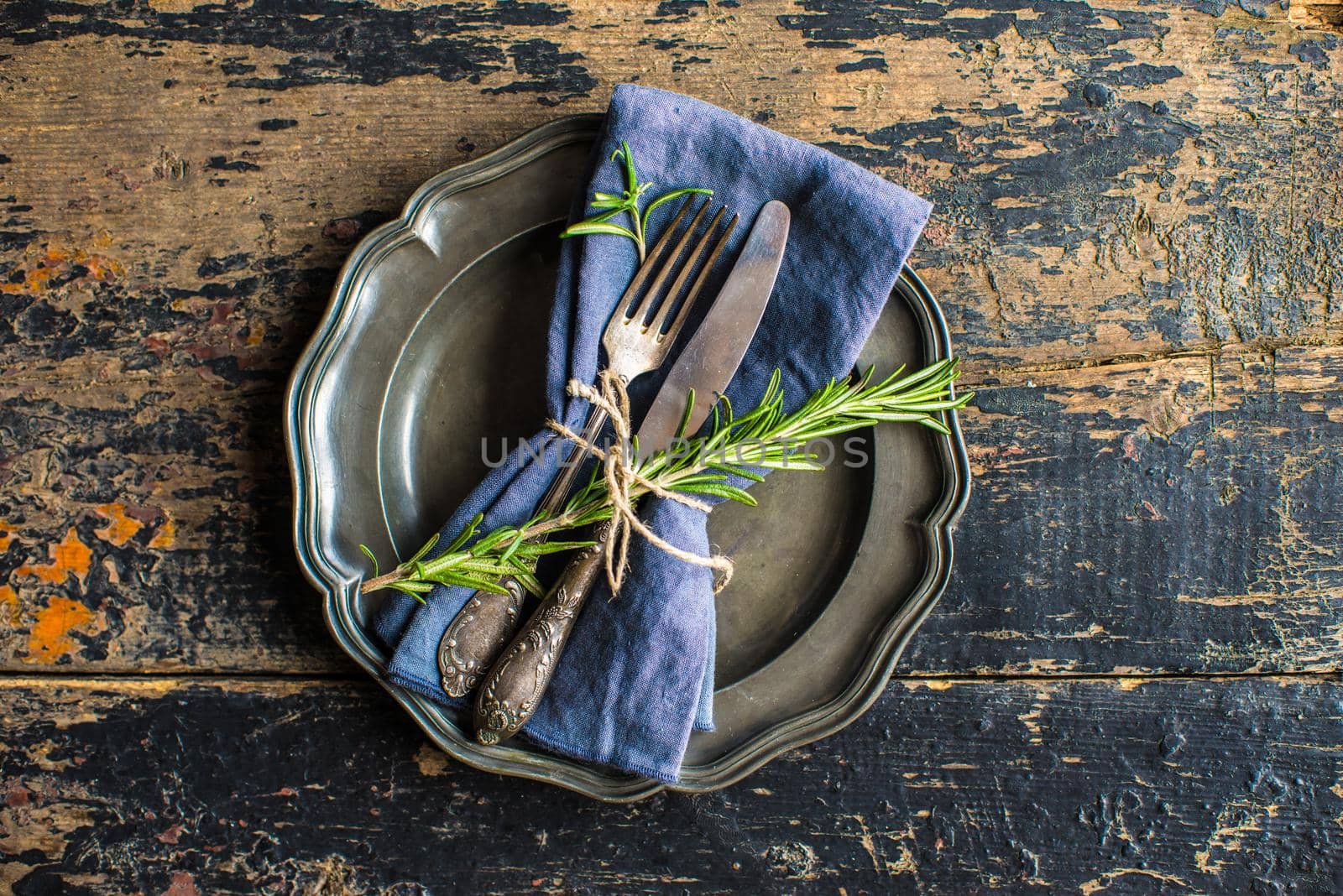 Rustic table setting with empty plate and vintage silverware decorated with fresh rosemary on dark wooden table