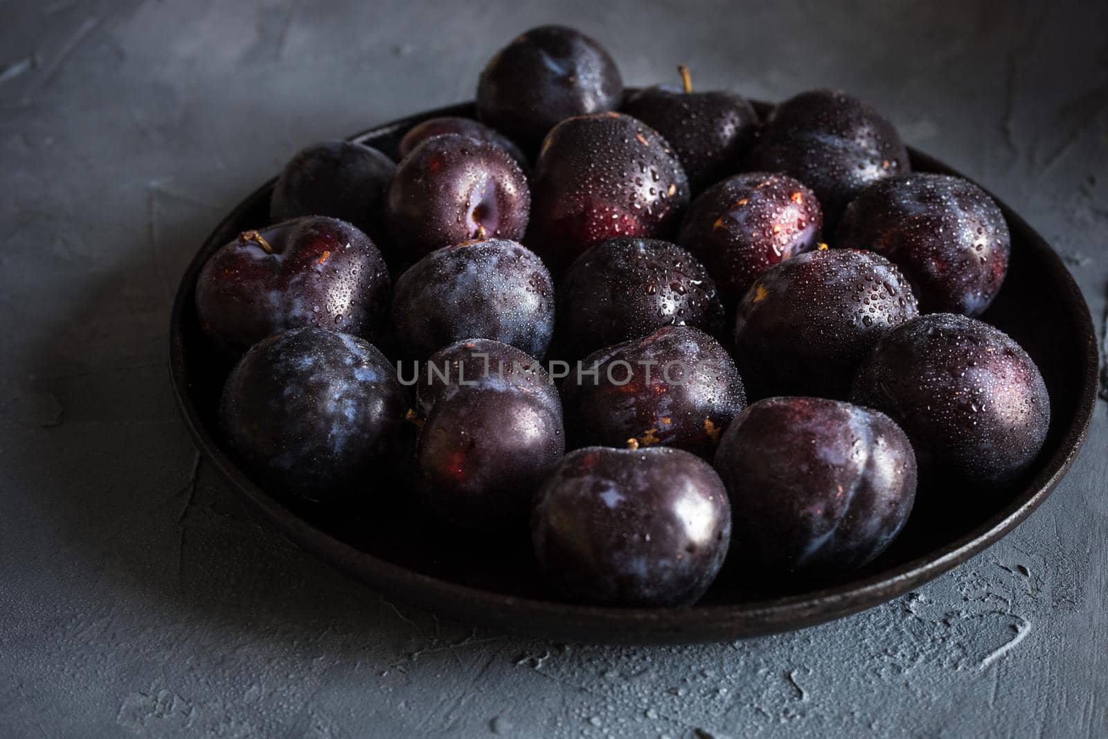 Fresh organic plums in a bowl on grey concrete background