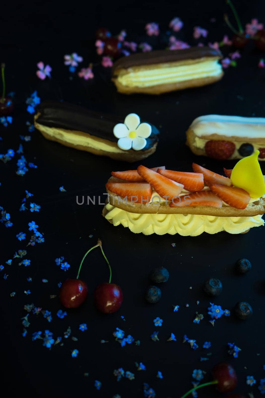 Different eclair dessert on dark wooden table decorated with strawberries and flowers