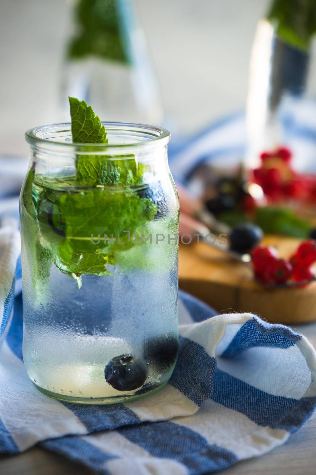 Detox summer drinks with fresh mint leaves and berries on white rustic wooden table