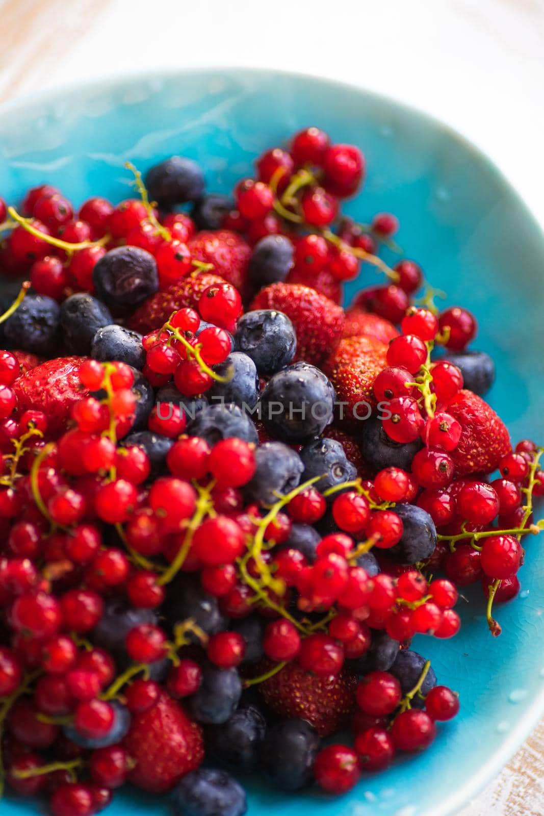 Plate with fresh organic berries - strawberry, blueberry (bilberry) and redcurrant on rustic wooden table with copyspace